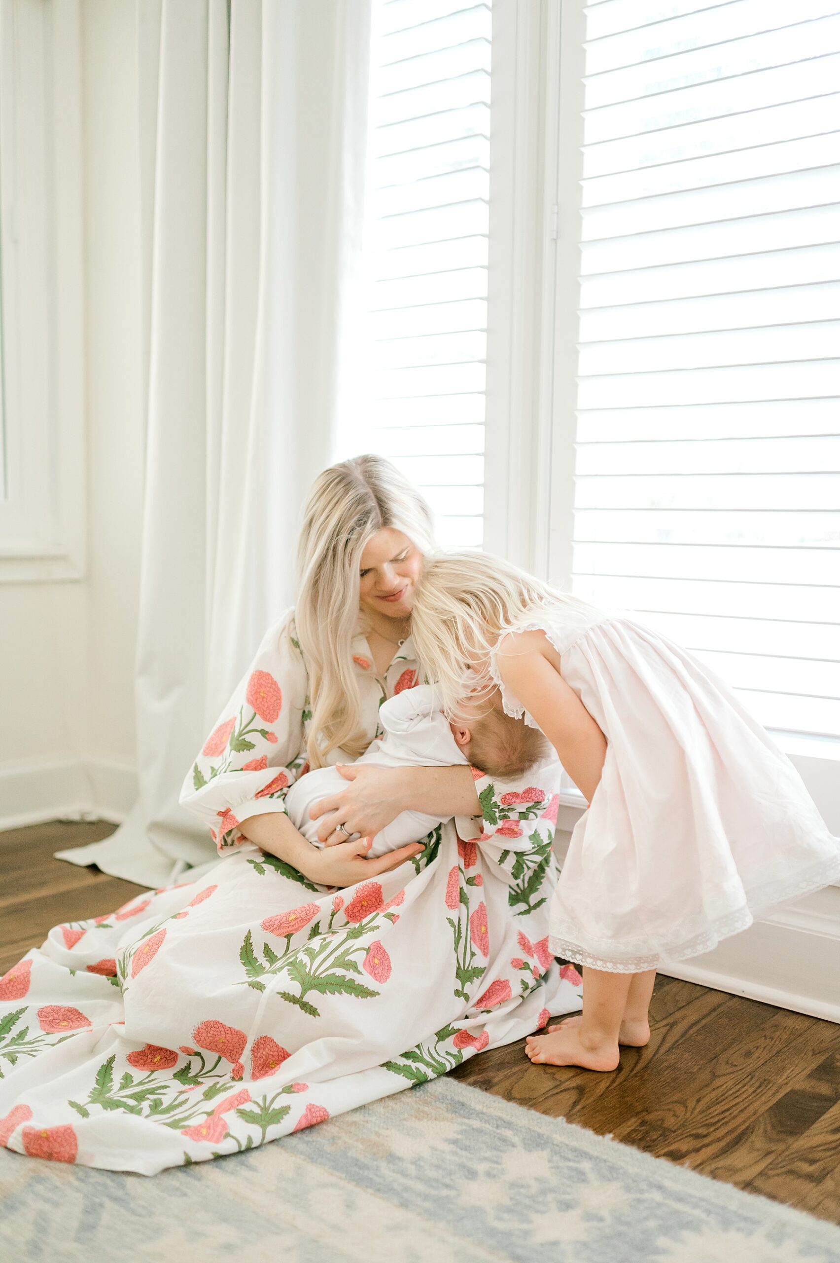 mom holds newborn while big sister kisses her on  the head