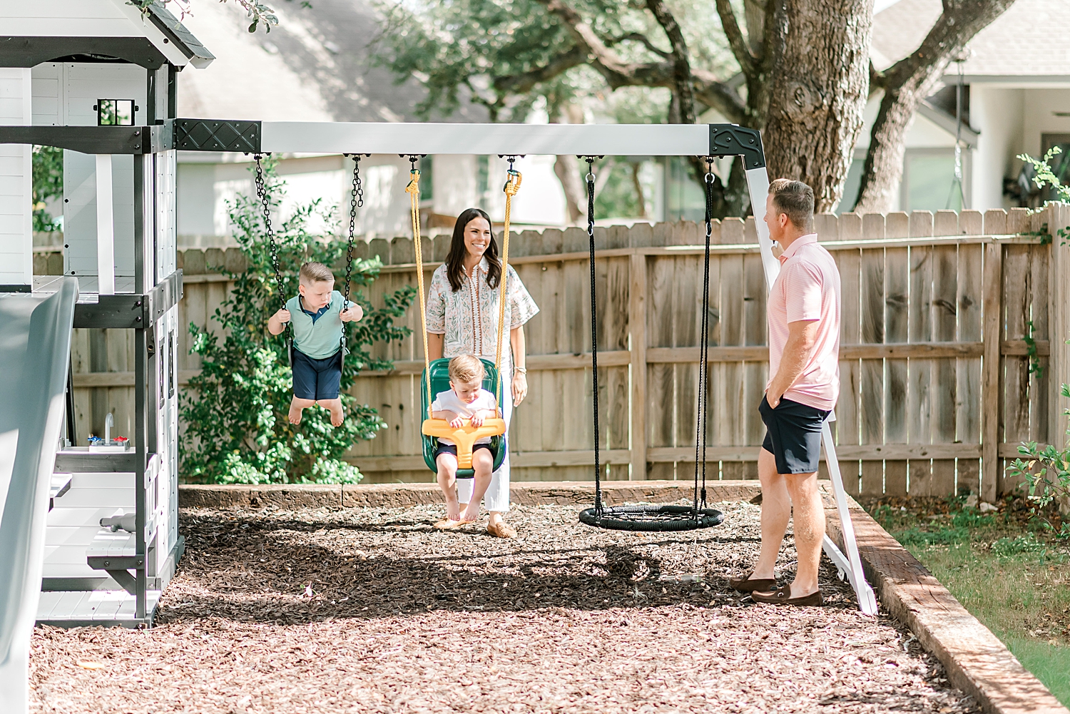 family plays outside as parents push kids on swings