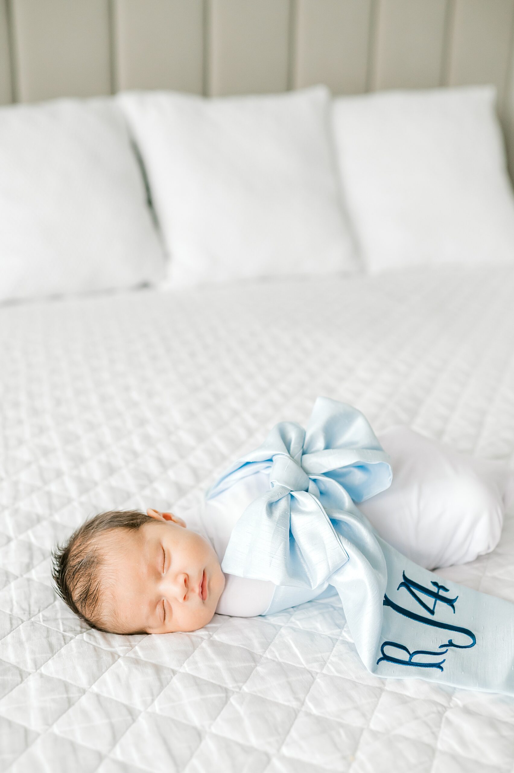 newborn boy sleeps soundly in white swaddle with baby blue wrap