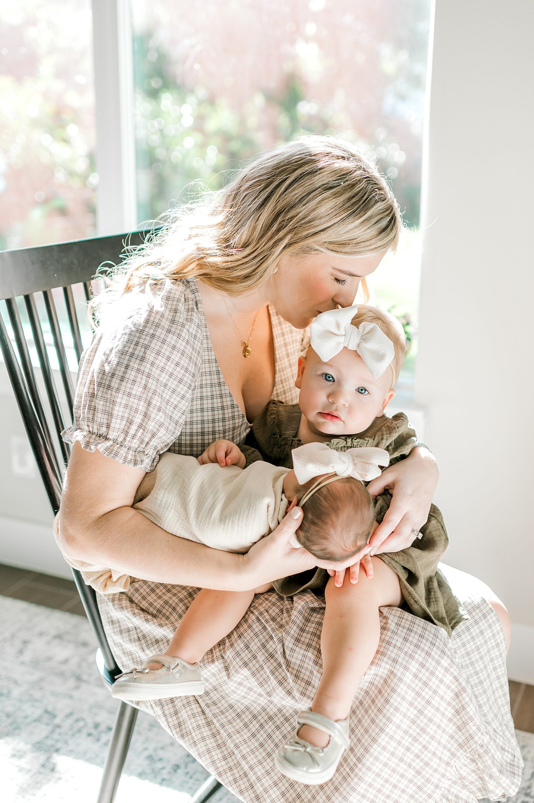 mom kisses older daughter's head while holding newborn