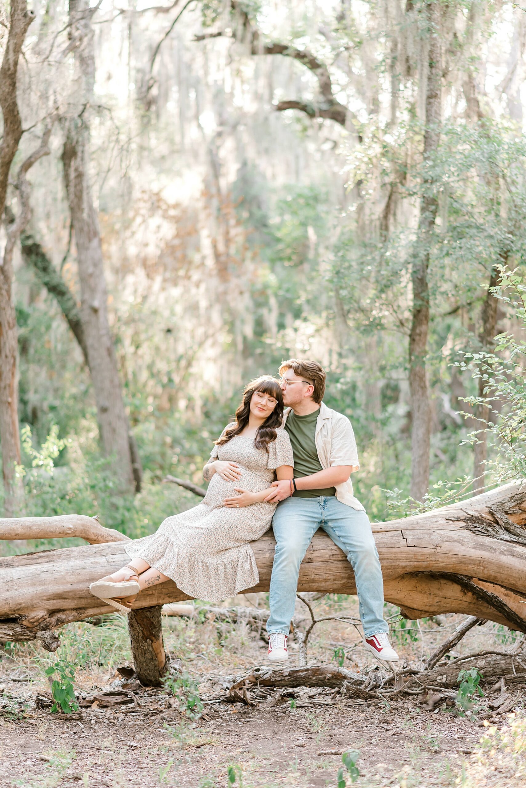 expectant parens sit on log during outside maternity portraits 