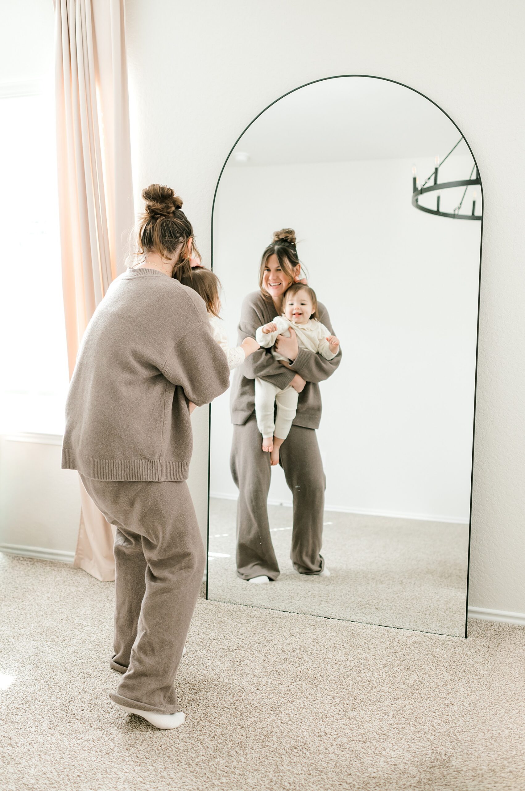 mom holds toddler girl while looking in the mirror 
