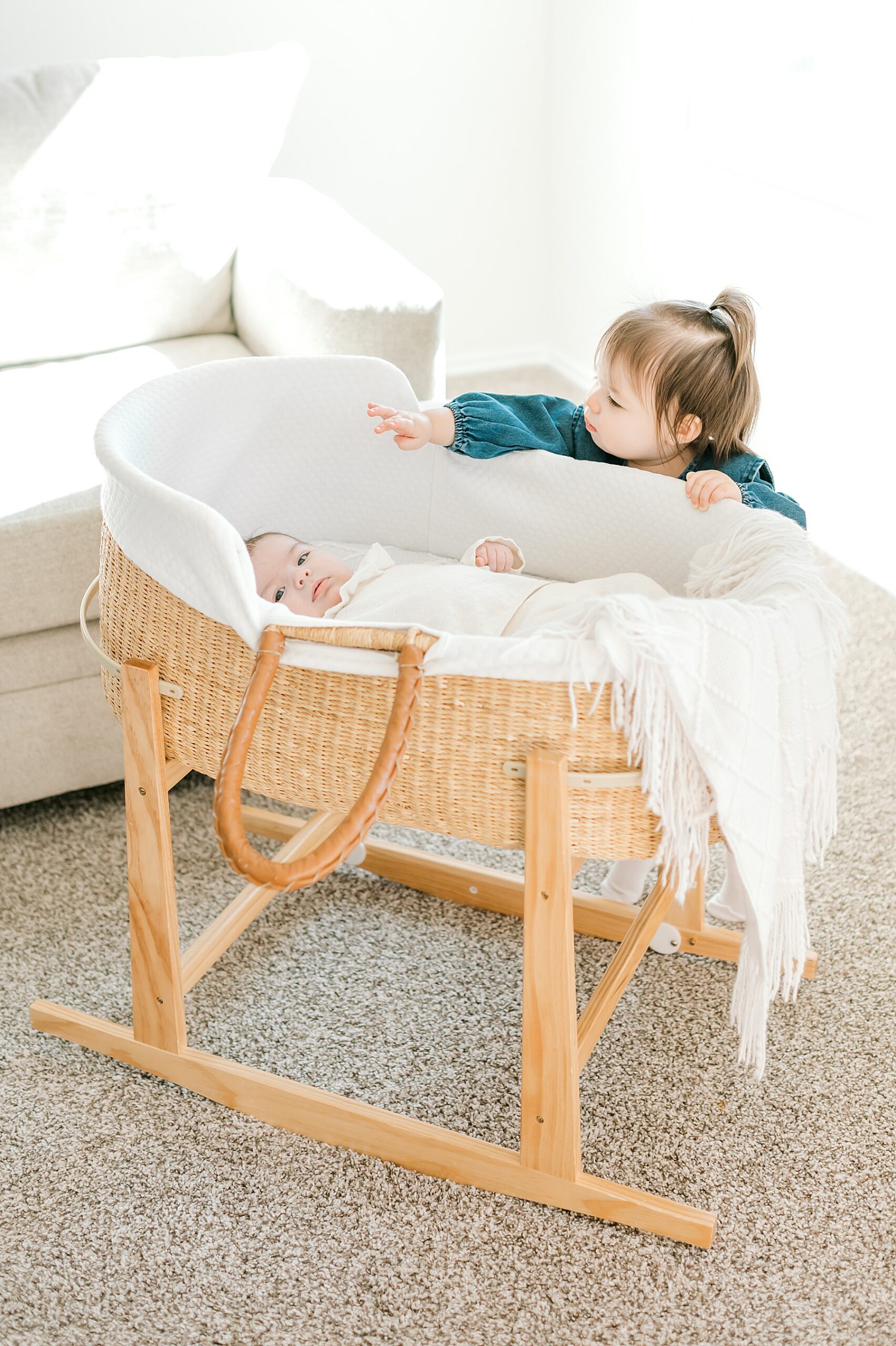big sister peeks in on newborn sister sleeping in bassinet 