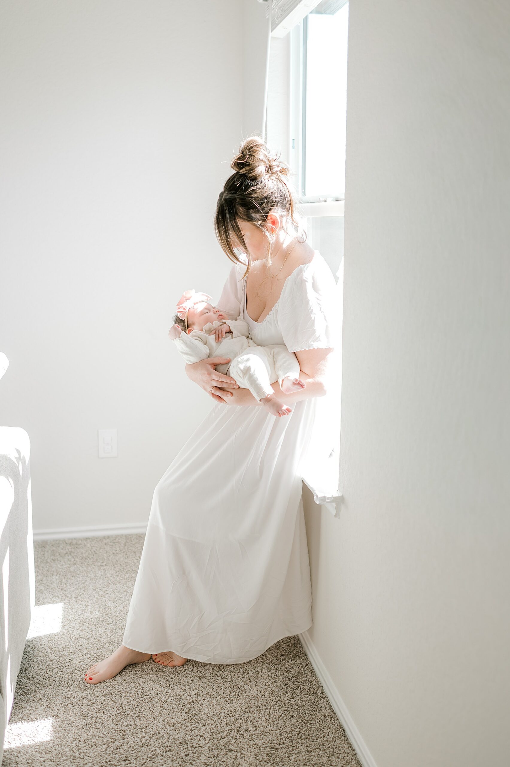 light and airy newborn portraits of mom holding newborn by window 